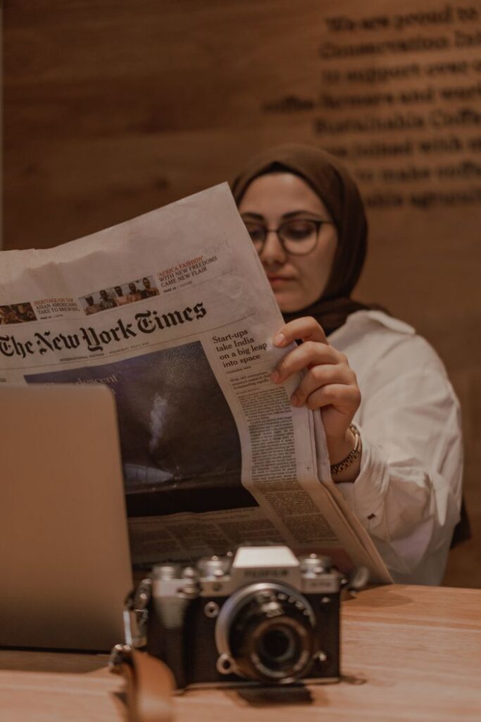 Mastering the First Impression: Your intriguing post title goes here Young woman in a hijab reads The New York Times in a warm café atmosphere, showcasing concentration and relaxation.